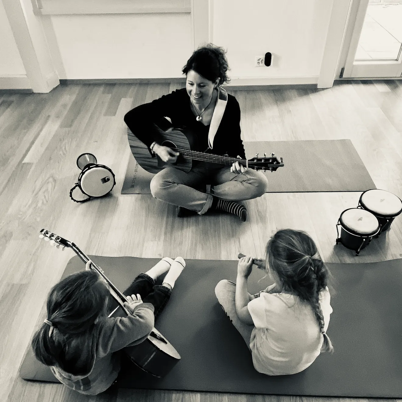 Laetitia joue de la guitare, assise au sol face à deux enfants, pendant un atelier d’éveil musical à Martigny