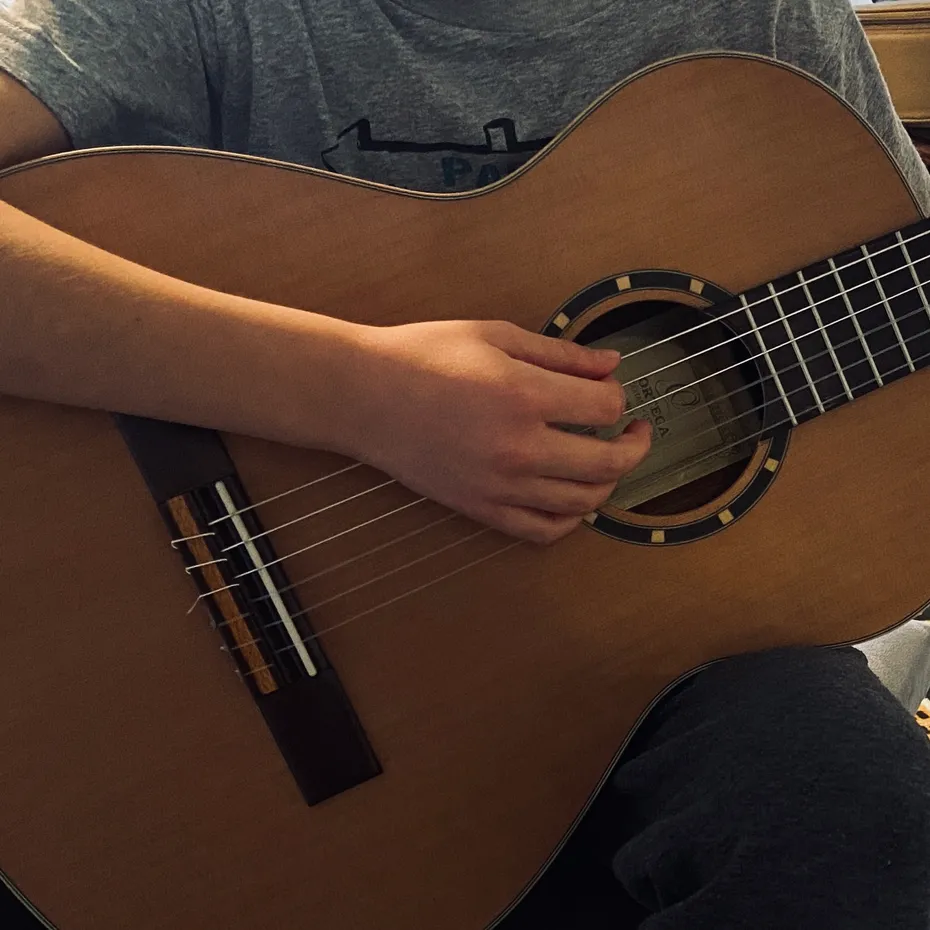 Un enfant joue de la guitare acoustique, assis, les doigts sur le manche