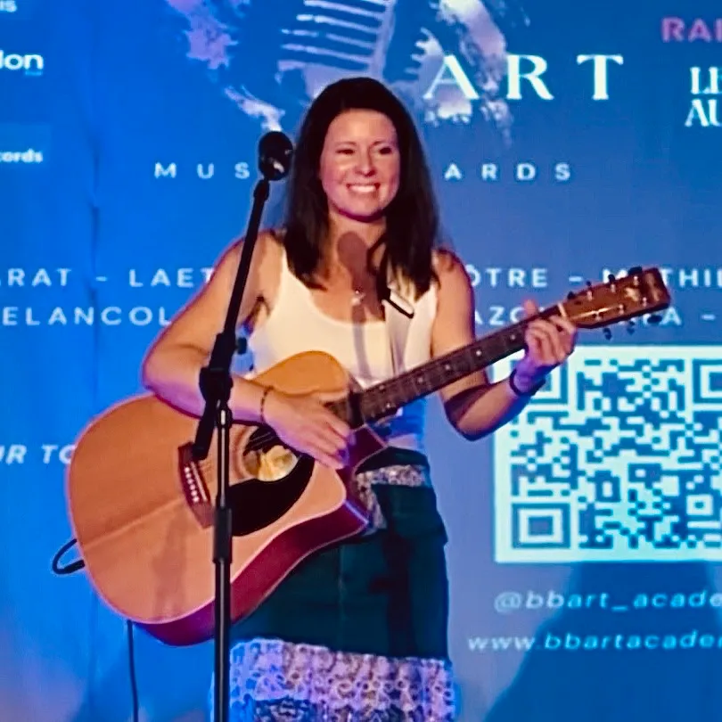 Laetitia Vuignier sur scène, guitare acoustique en main, devant un micro