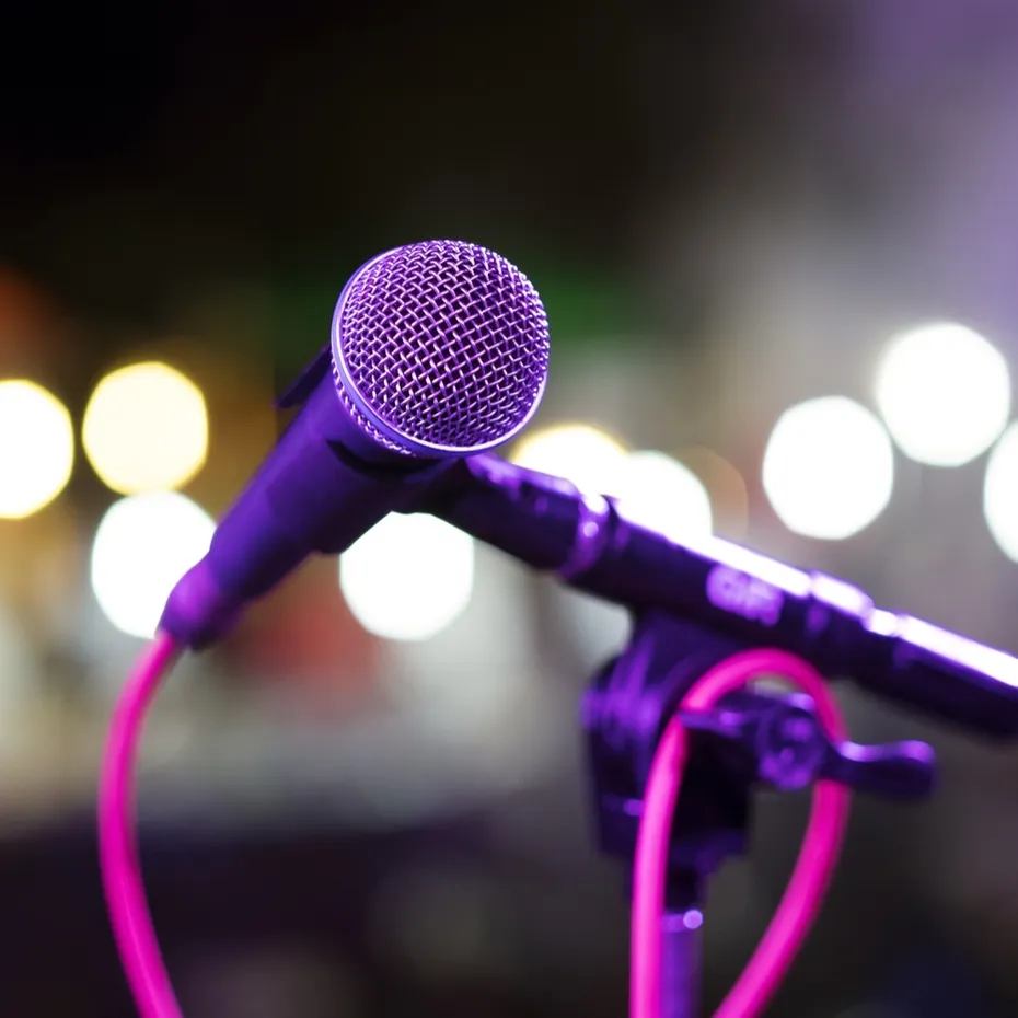 Un microphone sur son pied, éclairé en violet devant les lumières d’une scène
